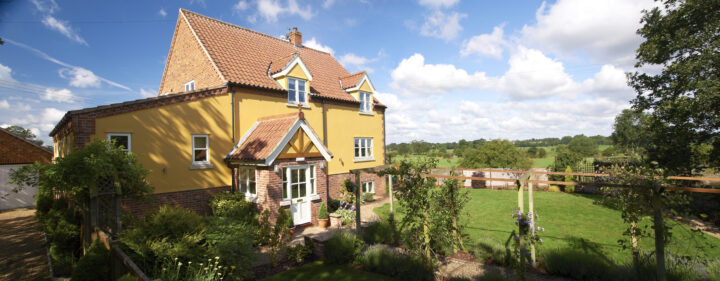 A yellow house with a green lawn and trees.